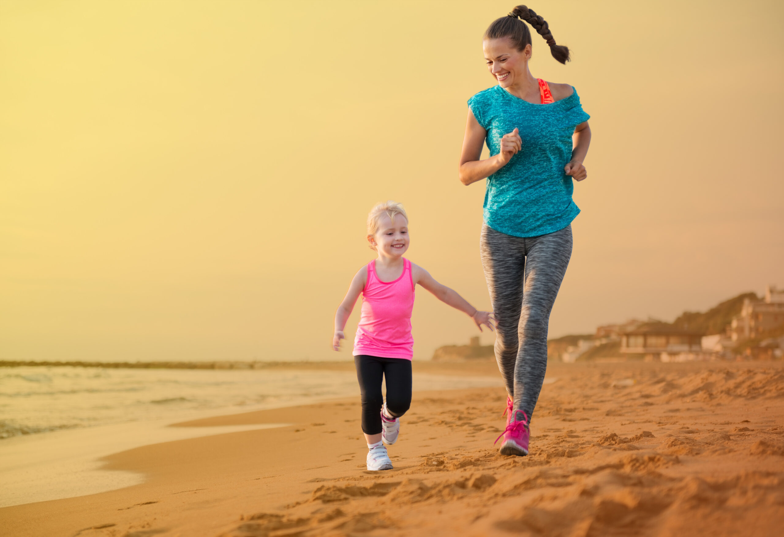 A woman and a girl run on the beach