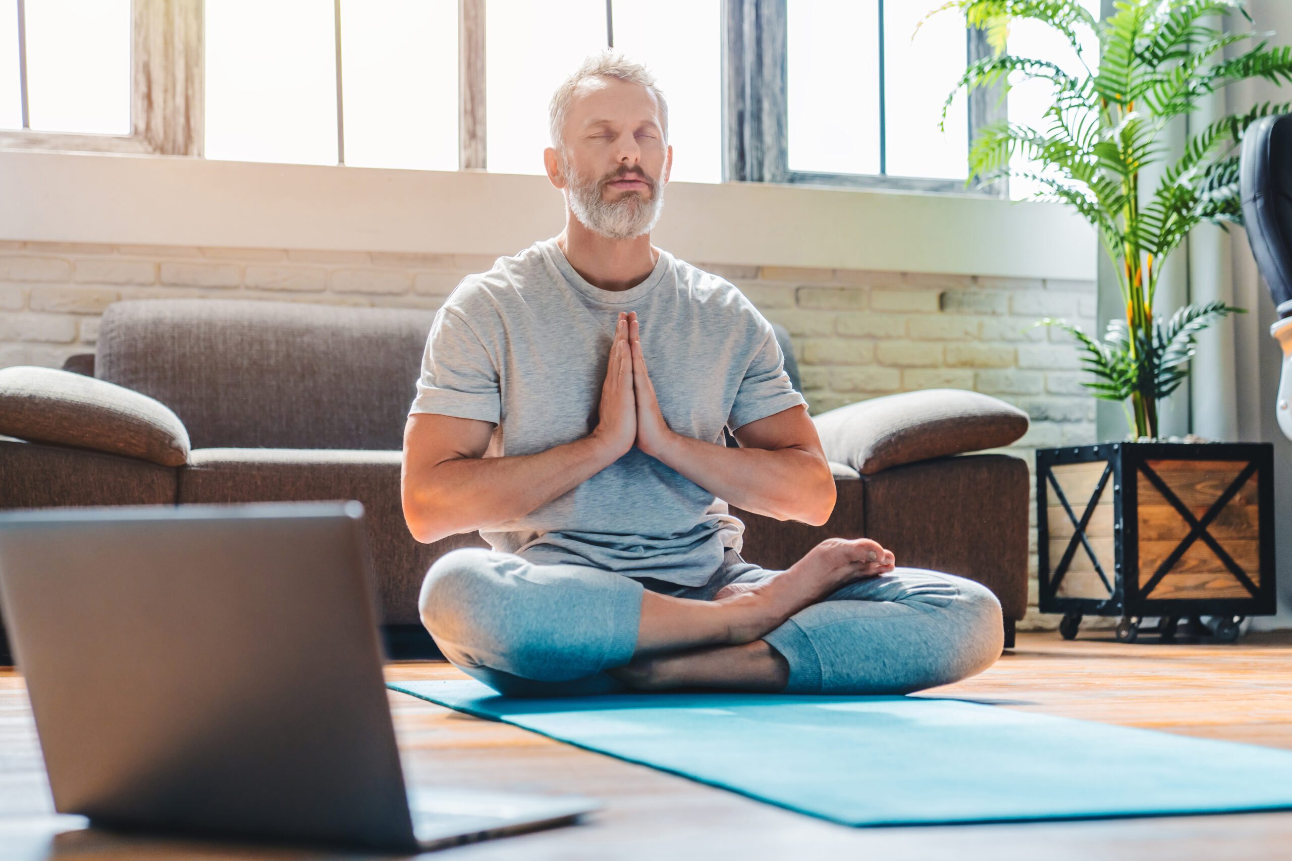 Portrait of middle aged sport man doing yoga and fitness at home using laptop