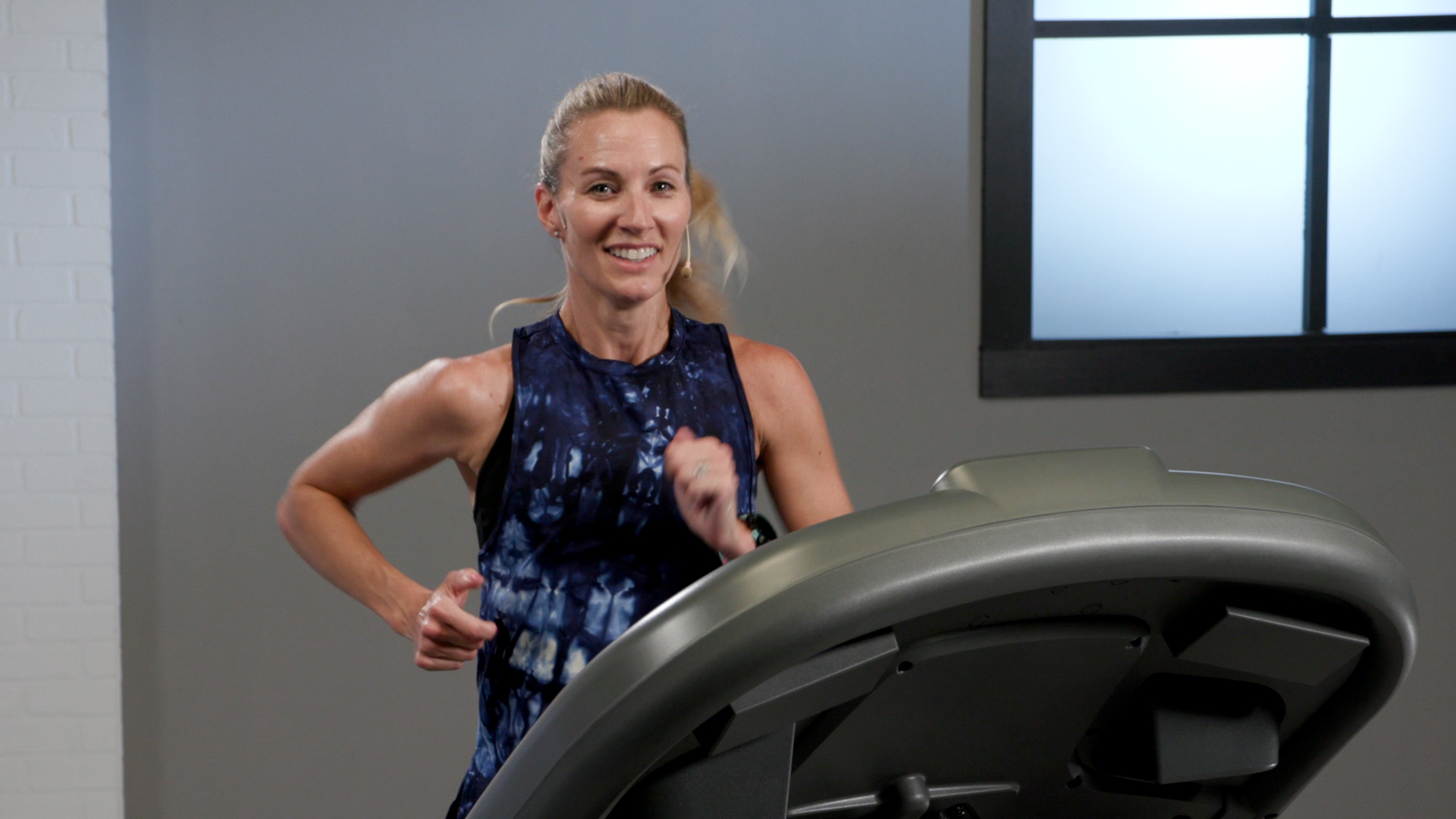 Wellbeats instructor Carrie T smiles while running on a treadmill