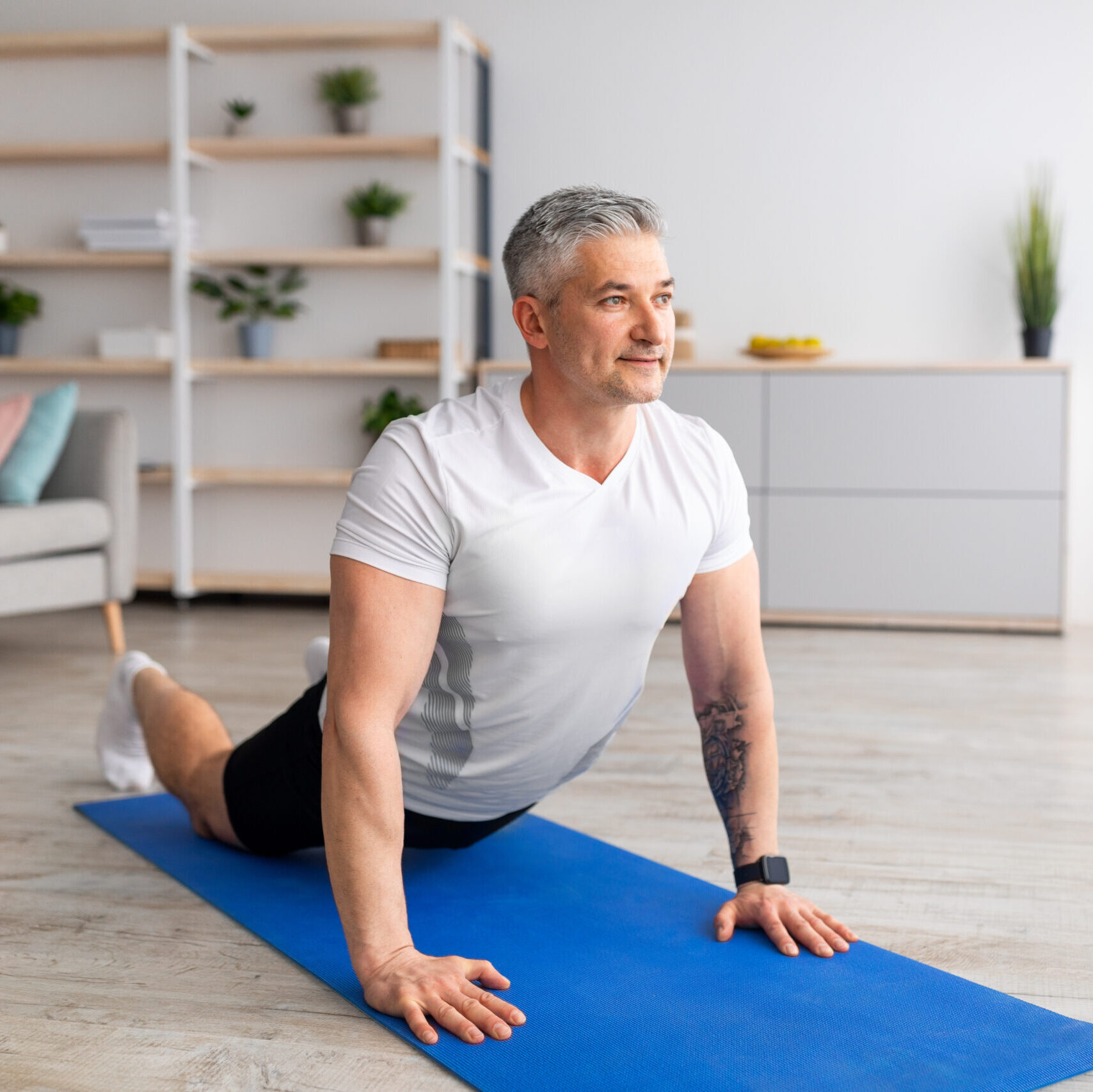 Mature man doing cobra pose, stretching back muscles, exercising in living room