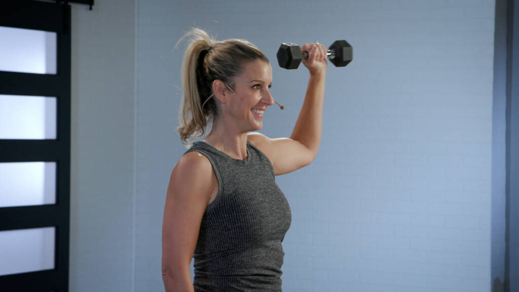 Wellbeats instructor Tina M. smiles while holding a single dumbbell in her left hand.