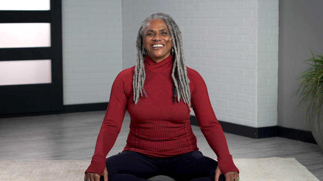 Wellbeats instructor Jan J. smiles while seated on a yoga mat