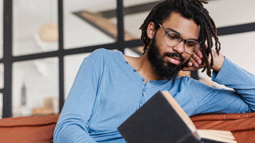 A man leans his head on his hand as he reads a book.