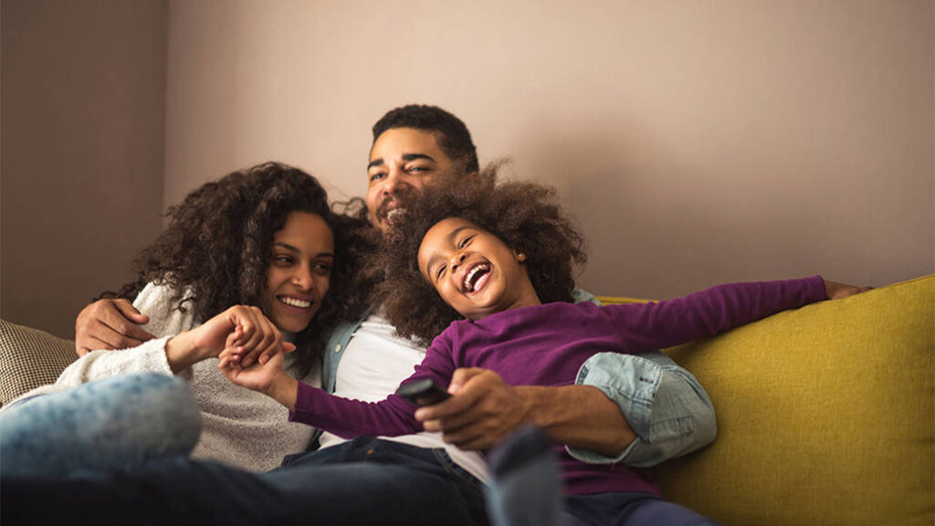 A family of three hugs sitting together on a couch.