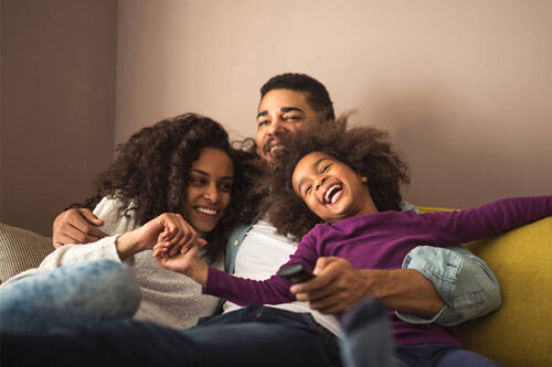 A family of three hugs sitting together on a couch.